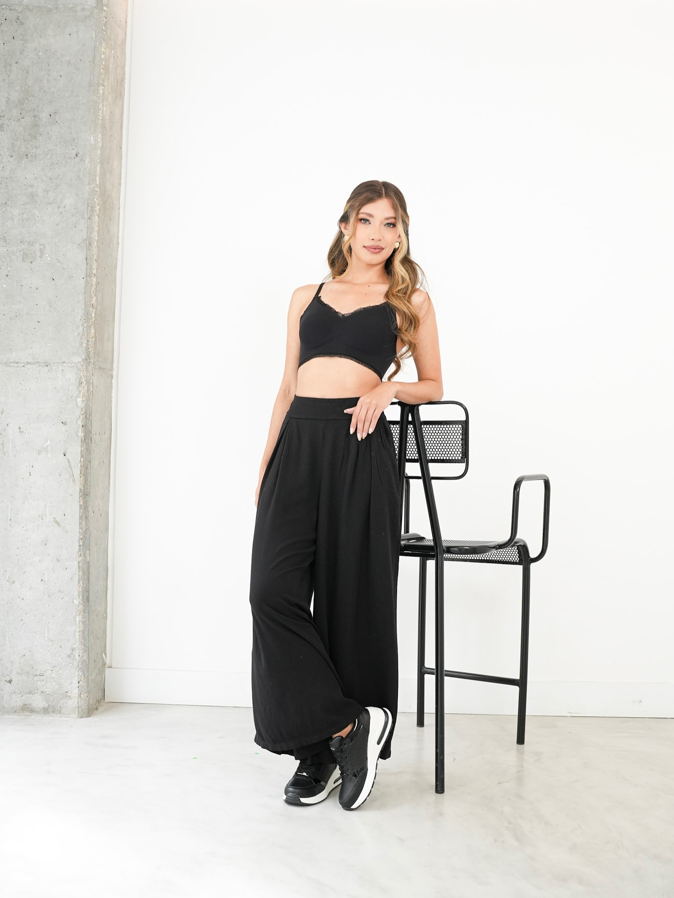 Fotografía de campaña de Opposite: modelo con conjunto negro y tenis junto a una silla alta.