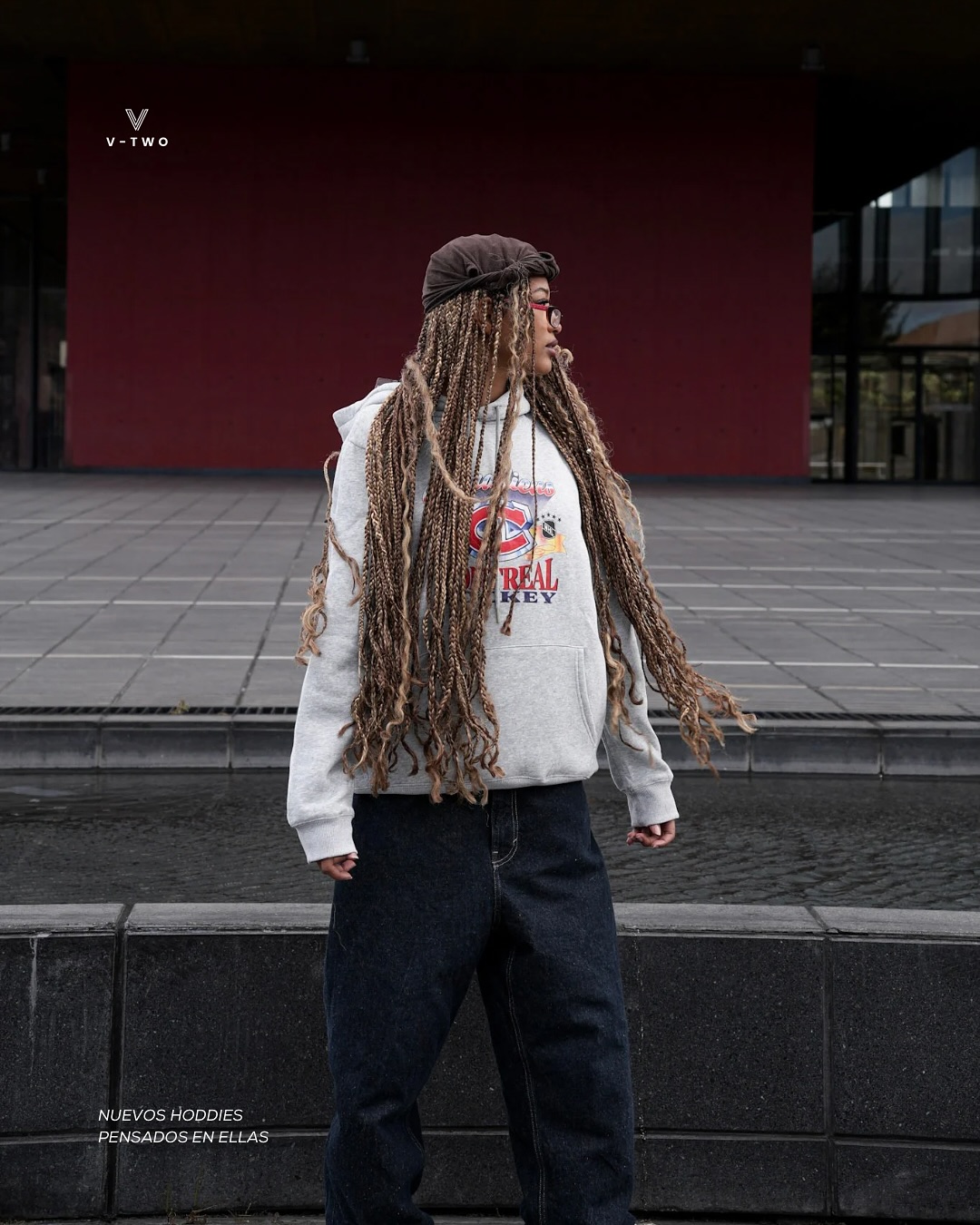 Fotografía de V-TWO Urban: modelo con hoodie gris frente a una fachada roja.